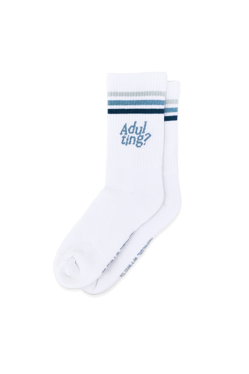 Calcetines blancos con rayas grises y azules en el borde superior. Estampado azul con la frase Adulting?